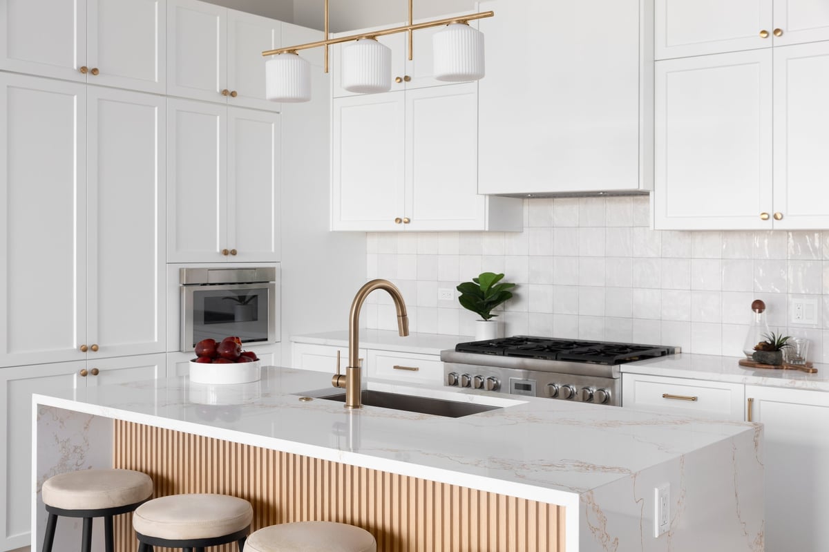 Kitchen detail with white cabinets, a waterfall marble countertop, wood slat panel, and gold light fixture and hardware