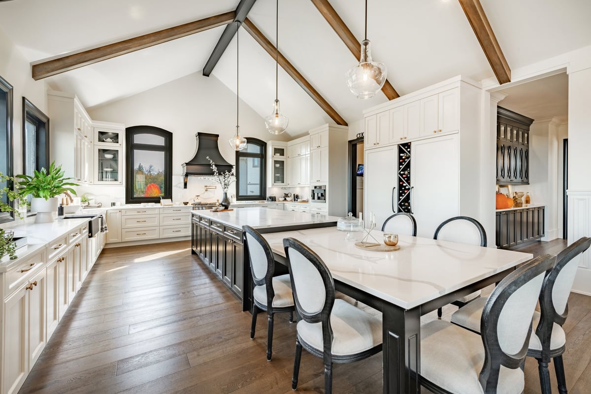 Expansive luxury kitchen with a long marble island, white stone countertops, dark wood cabinetry, and vaulted beam ceiling