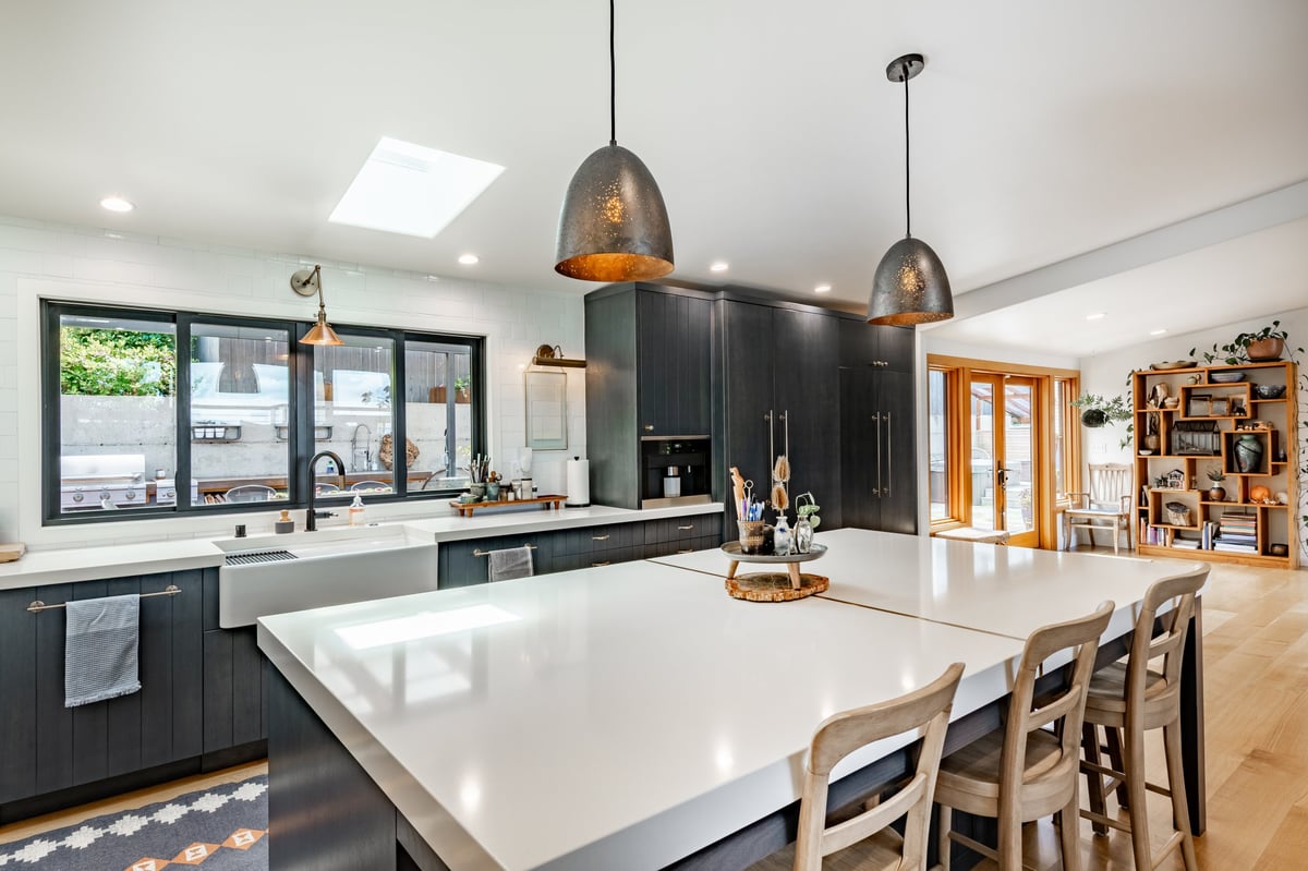 Open concept luxury kitchen with dark cabinetry, a large white island countertop, and hammered metal pendant lights