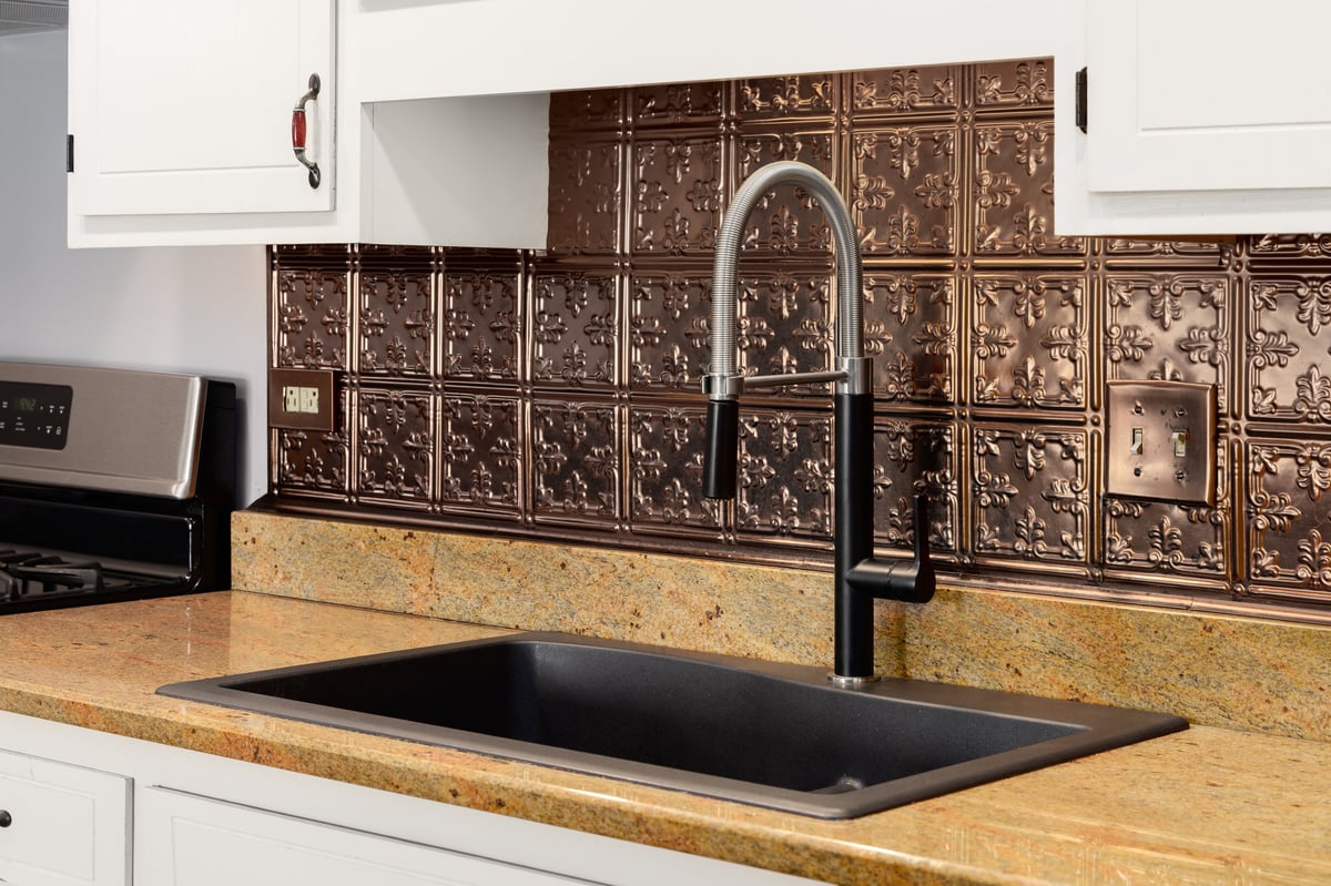 Kitchen faucet detail with white cabinets, a black ceramic sink, and a copper stamped backsplash