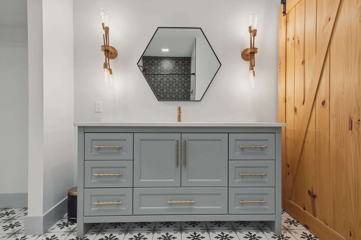 Modern bathroom with a stone vanity, hexagonal mirror, and gold sconces